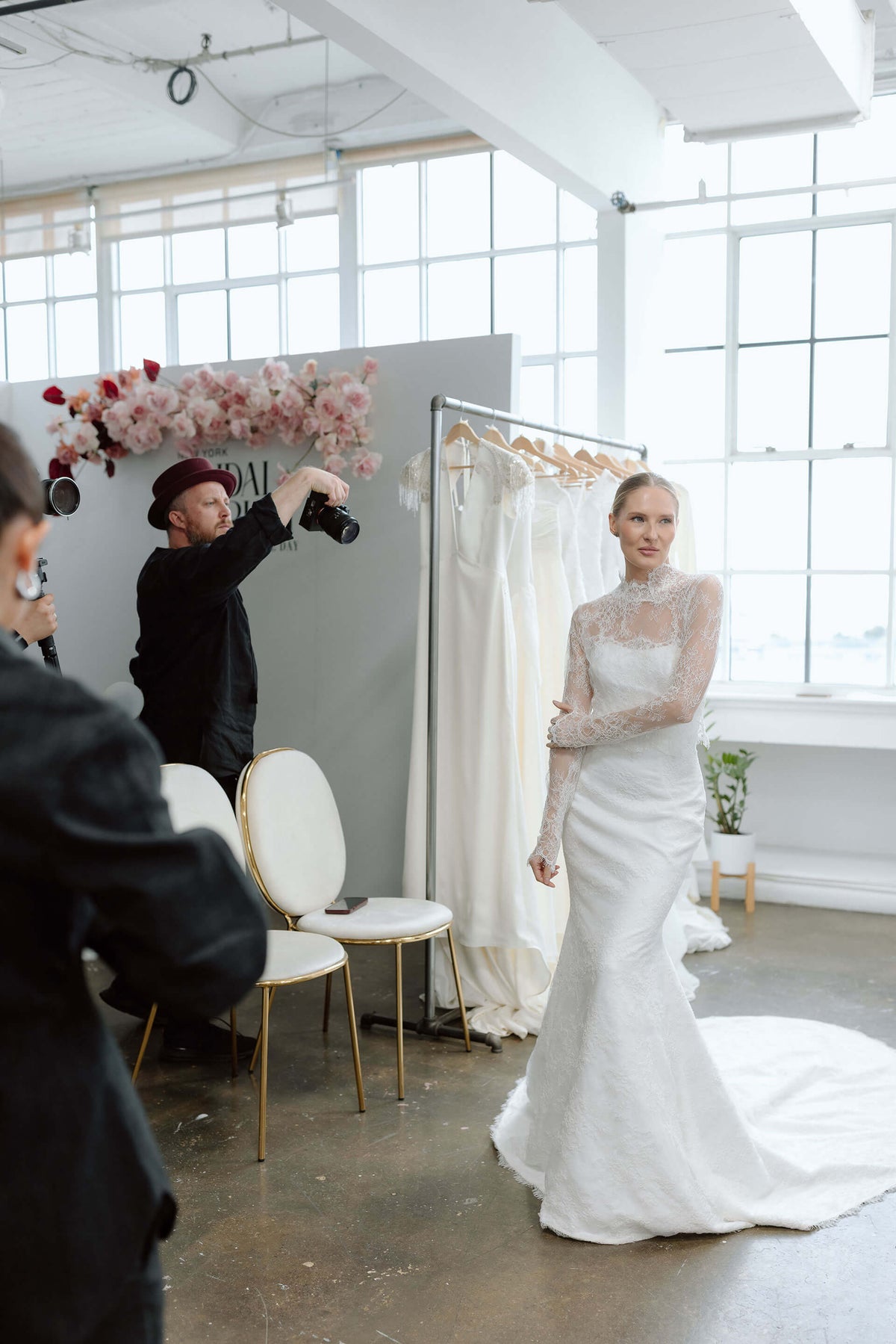 Model wearing a white wedding dress at the New York Bridal Market with a photographer taking pictures.