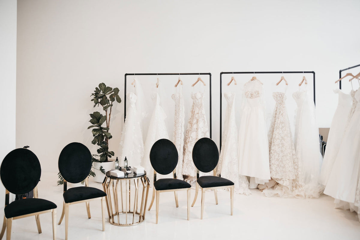 a bridal market designer showroom with racks of wedding gowns, and black tables and chairs