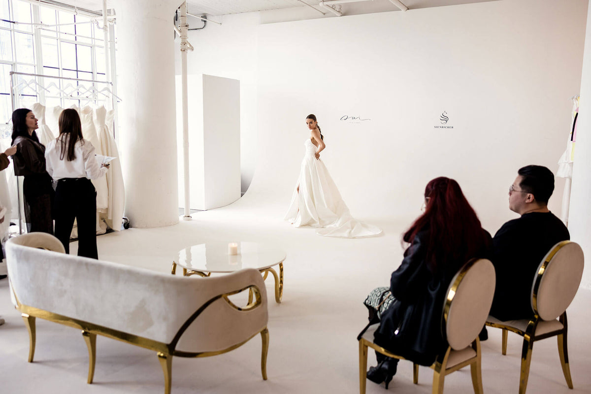 People observing a model of wedding dress  designed by sienricher in a white room with furniture.
