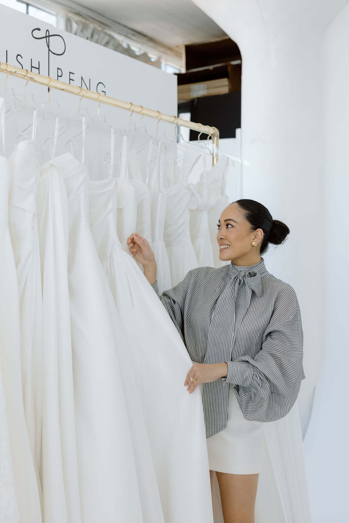 Woman selecting a white dress from a rack of wedding dresses by Trish Peng