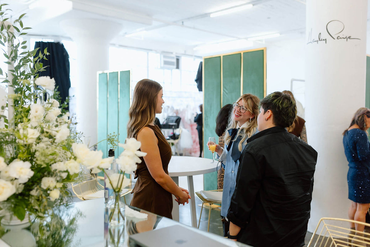 People socializing in a bridal trade show with green walls and white furniture.